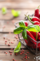 Red chili peppers with a sprig of basil in a wicker metal basket on a wooden background