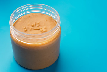 Obraz na płótnie Canvas Plastic jar with peanut butter on blue background