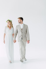 attractive bride and handsome bridegroom holding hands and looking away