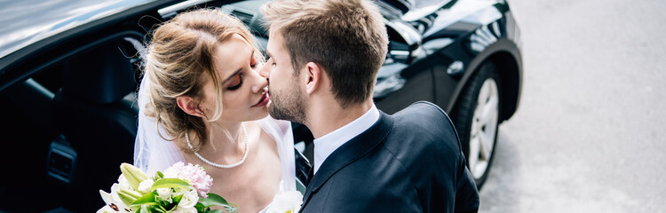 panoramic shot of attractive bride and handsome bridegroom kissing outside