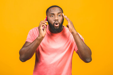 Fototapeta na wymiar Portrait of a amazed african american guy talking on mobile phone isolated against yellow background.