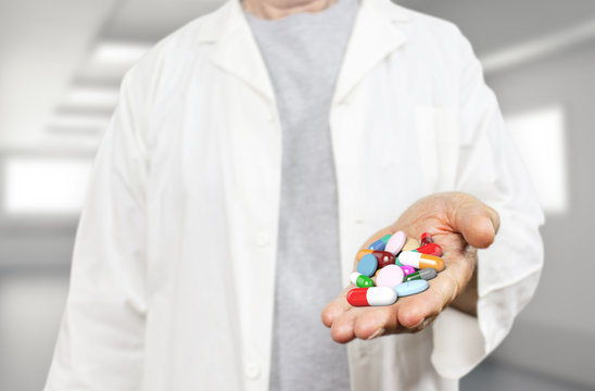 Old doctor holding pills, capsules, drugs and medics on a blurred hospital background 3d rendering. Medicine, health care, overmedication and disease healing concept.