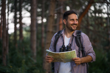 Adult man is hiking in forest. He is looking at map.