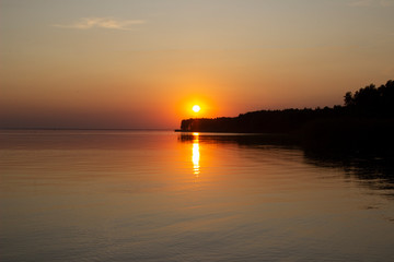 The  horizontal photo of golden sunset above the river or sea. Reflection in the water like fire. Seacoast.