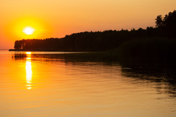 The  horizontal photo of golden sunset above the river or sea. Reflection in the water like fire. Seacoast.