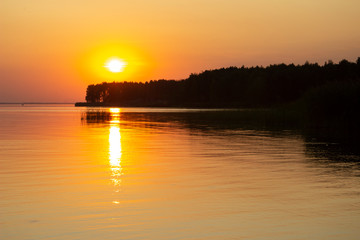 The  horizontal photo of golden sunset above the river or sea. Reflection in the water like fire. Seacoast.