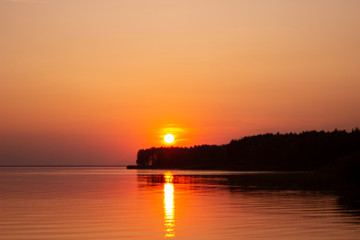 Fototapeta premium The horizontal photo of golden sunset above the river or sea. Reflection in the water like fire. Seacoast.