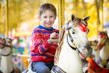 Fototapeta na wymiar Joyful child on a horse carousel. A handsome preschooler boy rides an amusement ride in an autumn park. Rest in the park