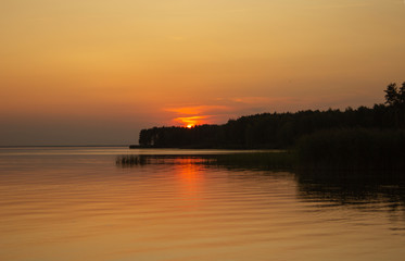 Fototapeta premium The horizontal photo of golden sunset above the river or sea. Reflection in the water like fire. Seacoast.