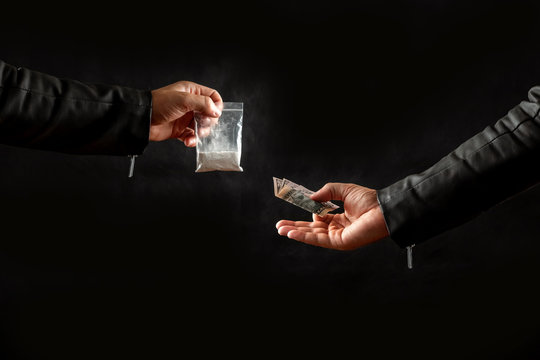 Hand of a drug addict with money, buying a dose of cocaine or another drug from a drug dealer on a black background. Social issue, drug addiction. Copy space.
