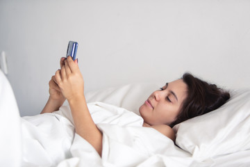 woman with smartphone in bed with white sheets