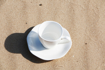 A cup of coffee stands on the sandy seashore
