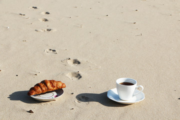 A cup of coffee stands on the sandy seashore