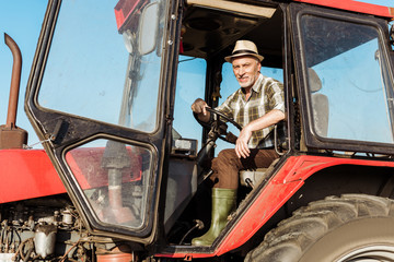 happy senior self-employed farmer in straw hat driving tractor