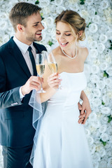 attractive bride and handsome bridegroom smiling and clinking with champagne glasses