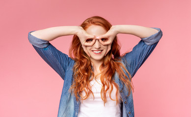 Playful redhead girl holding fingers near eyes like glasses