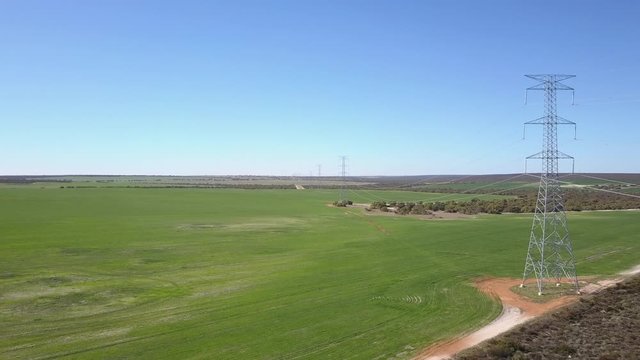 Aerial panoramic view of flight along high voltage power line in rural countryside of Western Australia, with blue sky and horizon as background.