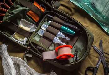 Open first aid kit with drugs and medical instruments on olive textile background. First aid in an...