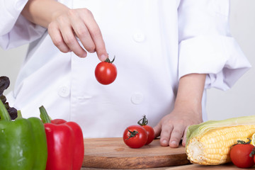Young woman chef choosing fresh ingredients for her cooking. Picking tometo on the wooden cutting board. Close up and clear lighting. concept for cooking or vegan food.