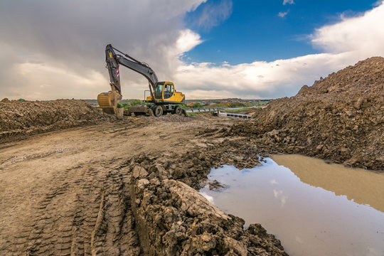 Excavator working in a construction site with puddles and mud