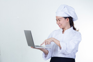 Young Asian woman chef using notebook computer. She is active of her career, researching for healthy foods or special recipes or education assignment. Half figured and studio lighting shooting.