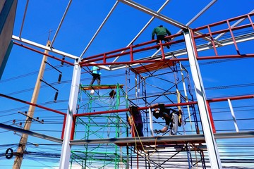 Low angle view of construction workers group on scaffolding are working to build building structure in construction site against blue sky background, occupation and construction concept