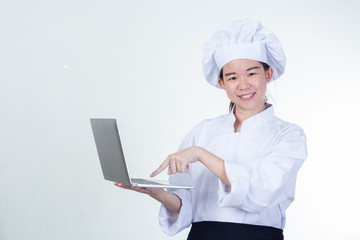 Young Asian woman chef using notebook computer. She is active and proud of her career, researching for healthy foods or recipes or education assignment. Half figured and studio lighting shooting.