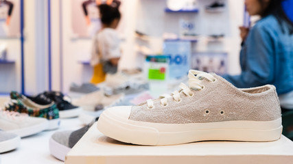 White sneakers on the display table in the fashion shoes store, close-up with blurred background of buyer. Costumers in shoes store with modern stylish pair close up.