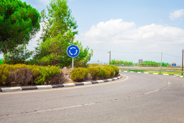 Rotonda con carretera y señal de la glorieta con arboles de pinos y arbustos con cielo azul