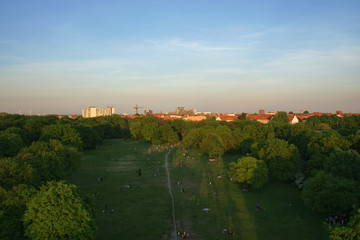 Aerial View of Berlin Park Hasenheide in Kreuzberg on an Spring afternoon with people relaxing and having fun on a large meadow in the sun. Behind the trees you can see roof tops of Berlin