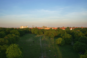 Aerial View of Berlin Park Hasenheide in Kreuzberg on an Spring afternoon with people relaxing and having fun on a large meadow in the sun. Behind the trees you can see roof tops of Berlin