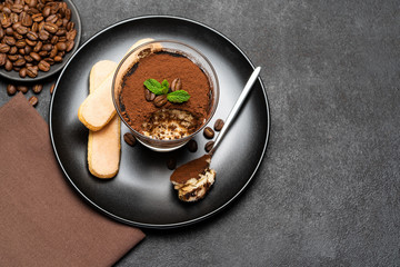 Portion of Classic tiramisu dessert in a glass cup on dark concrete background