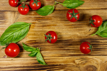 Fresh cherry tomatoes with green basil leaves on a wooden table. Top view