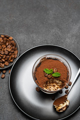 Portion of Classic tiramisu dessert in a glass cup on dark concrete background