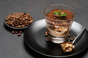 Portion of Classic tiramisu dessert in a glass cup on dark concrete background