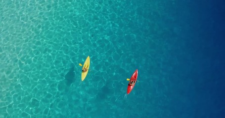 Aerial view of adventurous couple ocean kayaking together in pristine blue lagoon with sunny light textures refracting on the water surface, leisure kayaking tourism