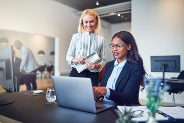 Two smiling businesswomen working on a laptop in an office