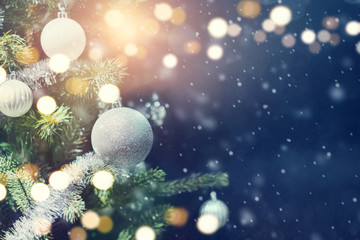 Christmas holiday background. Silver bauble hanging from a decorated on tree with bokeh and snow, copy space.