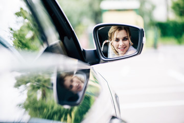 reflection of attractive and blonde bride looking at mirror in car