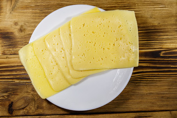 Slices of cheese in a plate on wooden table. Top view