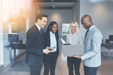 Diverse businesspeople using a laptop while standing in an offic