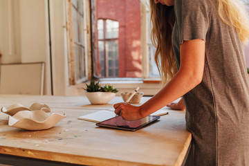 Side view of unrecognizable ceramic artist sketching on digital tablet at desk