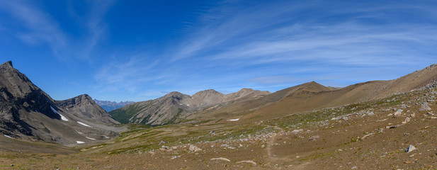 Hiking trail through a panoramic Rocky Mountain landscape with a white clouds, mountains and hills.