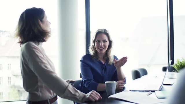 A group of business people with laptop sitting in an office, talking.