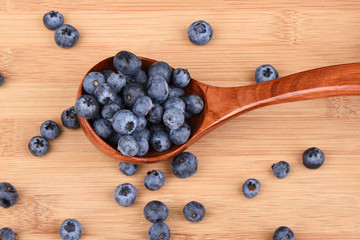 Blueberry berries in a wooden spoon on a wooden background.