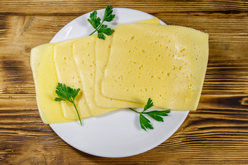 Slices of cheese in a plate on wooden table. Top view