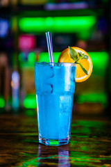 Blue cocktail in a high glass glass with a slice of orange. Colourful cocktail on the dark back. Cocktail on a Colourful  background in a tall glass.