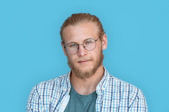 Young Bearded Handsome Man Blond Hair Hipster Face Wearing Optical Glasses Looking At Camera, Millennial Handsome Casual Guy Isolated On Blue Studio Blank Background, Close Up View Headshot Portrait