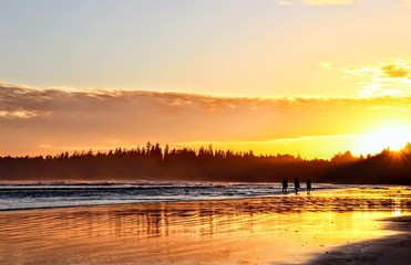 Obraz premium Silhouette people walking on the beach during the sunset at the edge of the ocean, surrounded by mountains