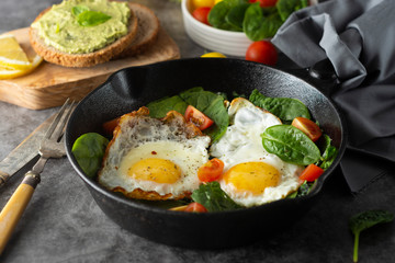 Fried sunny eggs with spinach, avocado toast and fresh tomatoes. healthy breakfast food.